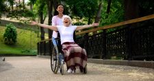 Long-Term Happiness. Picture of an elderly caucasian smiling female in a wheelchair, being pushed by a younger smiling asian female.